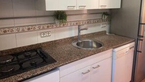 Una cocina con armarios blancos, encimera de granito, pileta de acero inoxidable, estufa y lavavajillas.