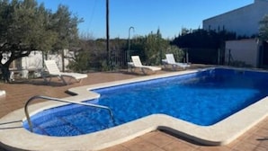 Una piscina rectangular con solárium empedrado, rodeada de sillones de descanso y un árbol.