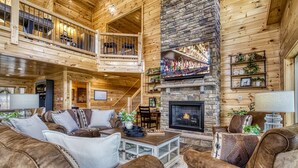 A spacious log cabin interior with a fireplace, wooden furniture, and a balcony. - Top Notch Lodge- Private Indoor Pool, Theater, Stunning Mountain Views (Pigeon Forge)