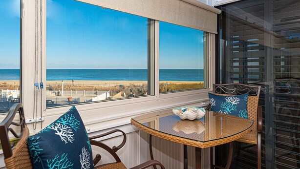 Une pièce avec une table et des chaises en verre, une vue sur la plage et une grande fenêtre.