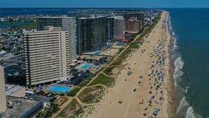 Un paysage urbain côtier avec de hauts immeubles, une plage parsemée de parasols et un ciel bleu dégagé.