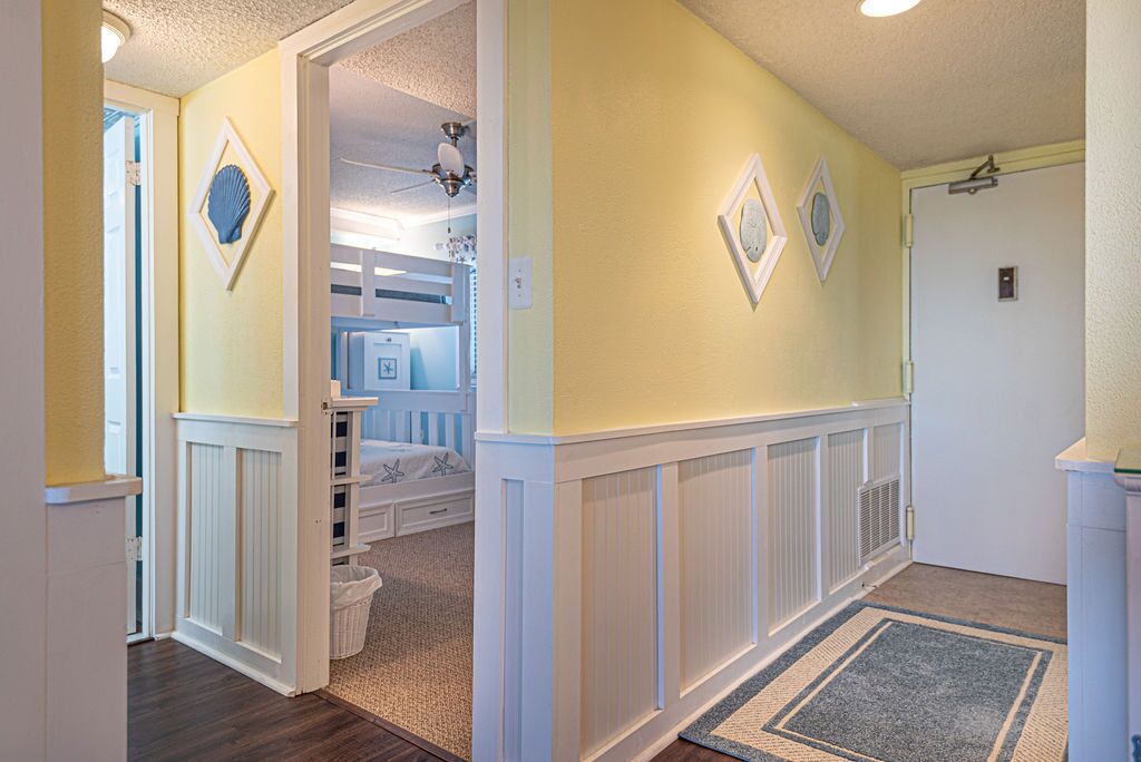 A hallway with a white wainscoting, a blue and white striped door, and a door with a white frame.