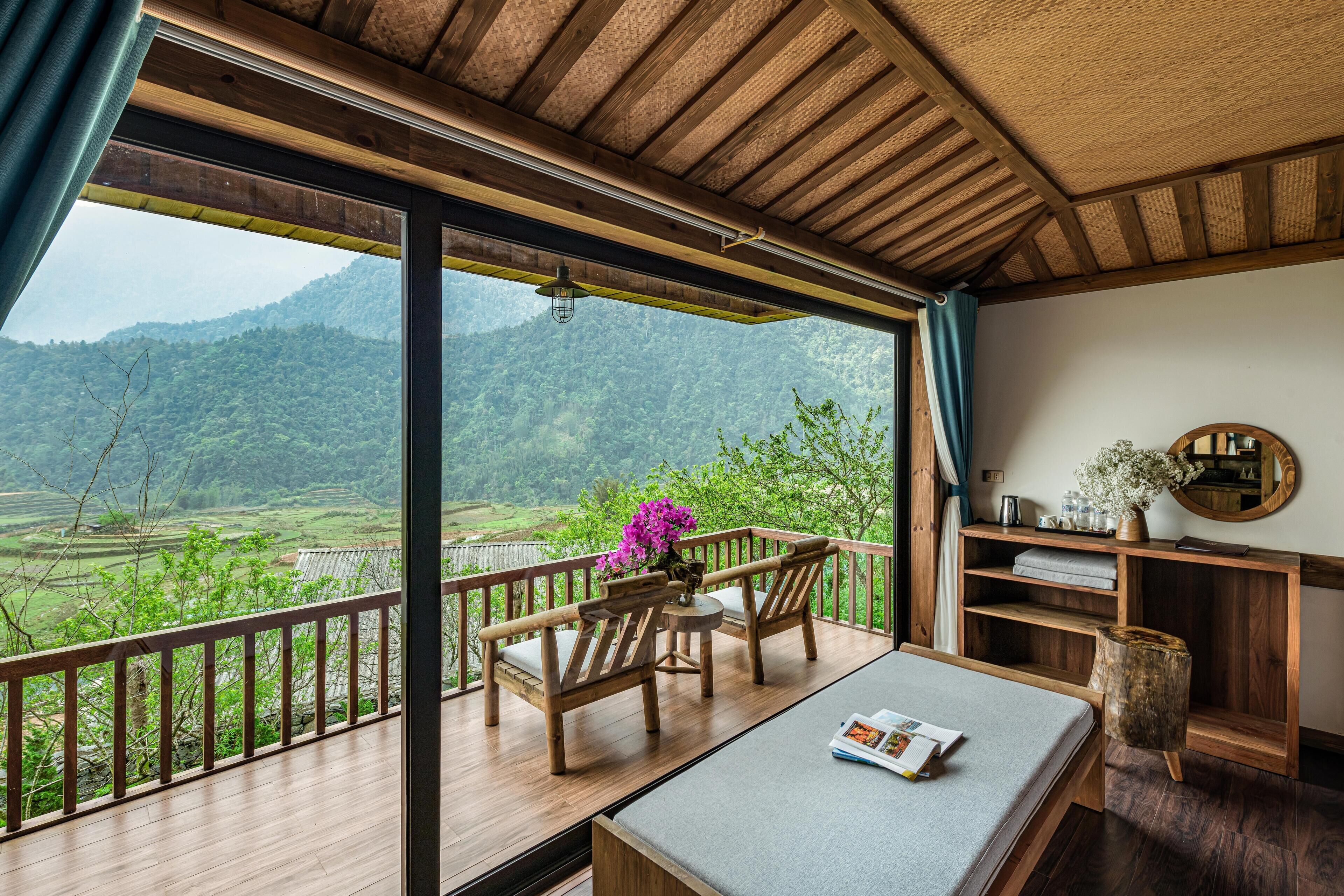 A wooden deck with a view of green hills, a wooden table with a magazine, and a small wooden stool.