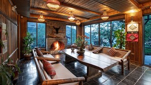 Un interior acogedor con chimenea de piedra, muebles de madera y ventanas amplias que ofrecen vistas al exterior.