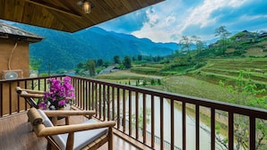 Un balcón de madera con vistas a campos escalonados y montañas.