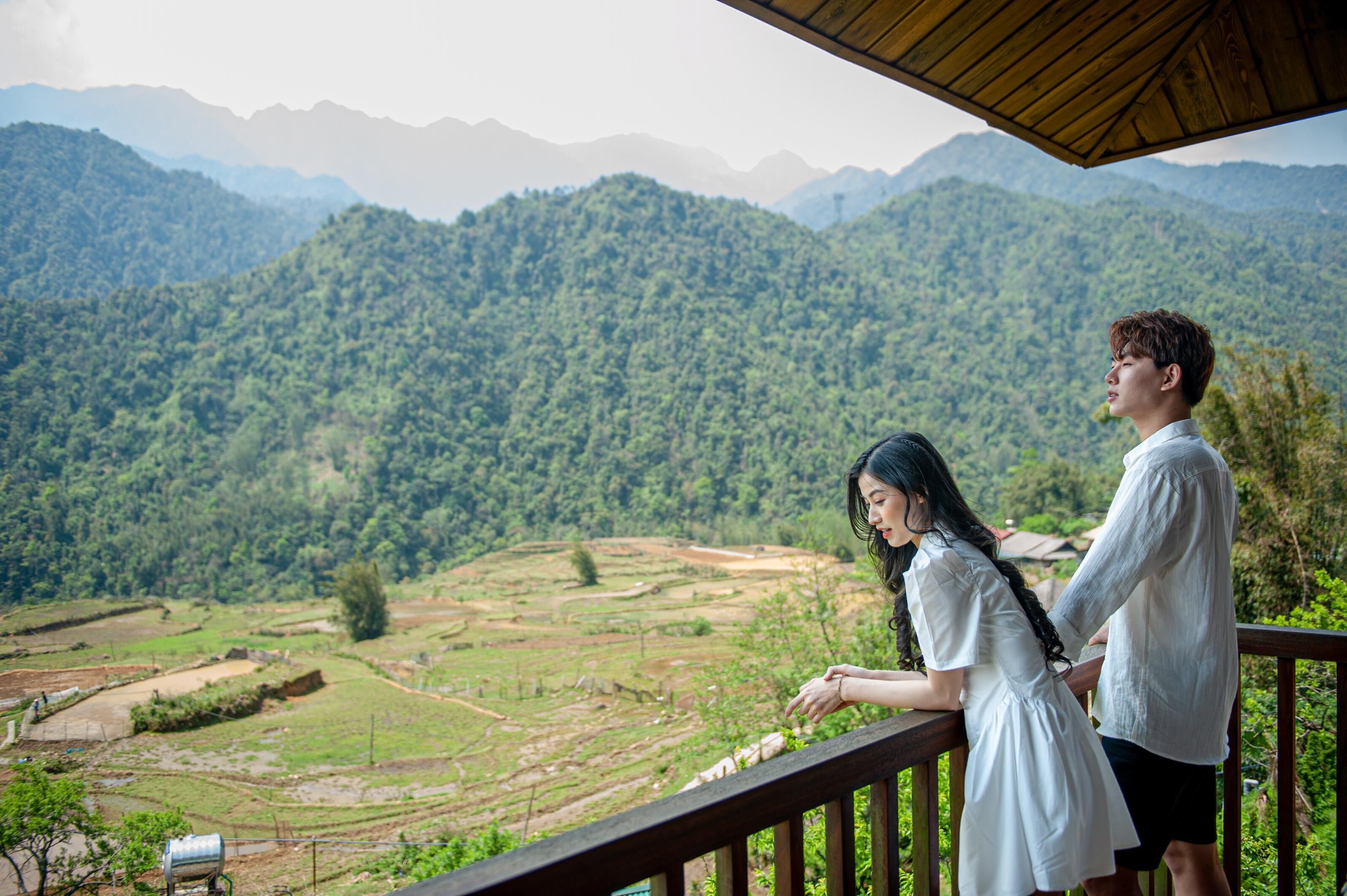 Un couple se tient sur un balcon en bois, d’où l’on peut admirer des champs en terrasses et des montagnes.