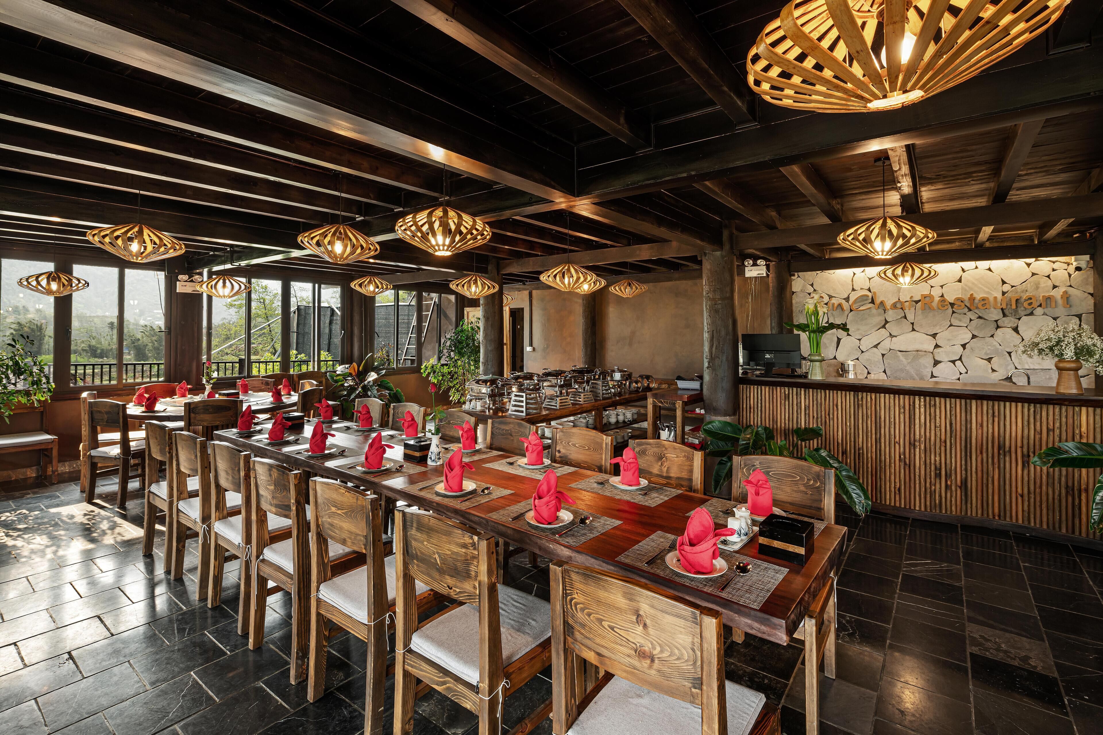 Un restaurant avec des tables et des chaises en bois, de grandes suspensions et un mur de pierre en arrière-plan.