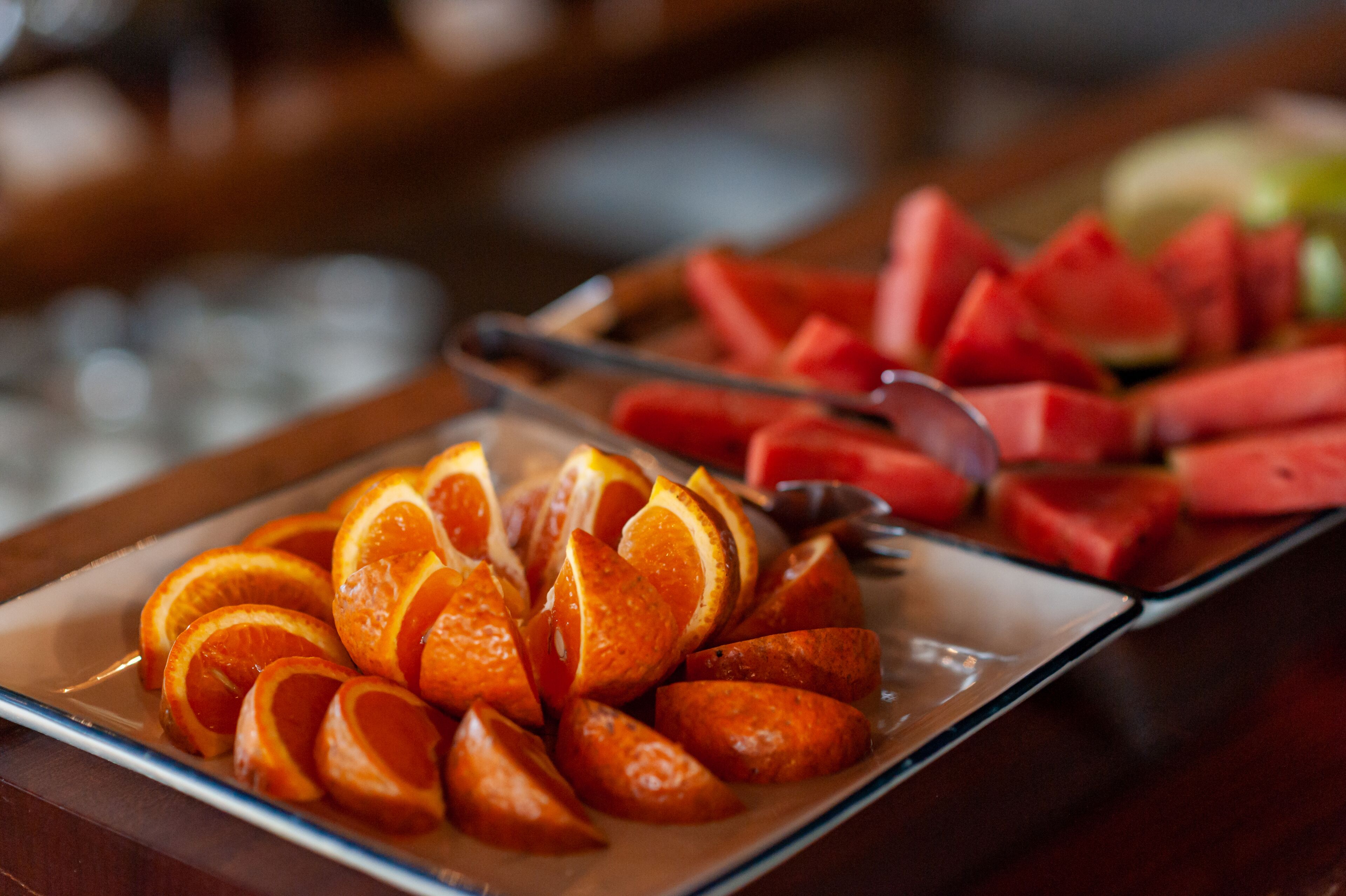 A tray with sliced oranges and watermelon on a wooden table.