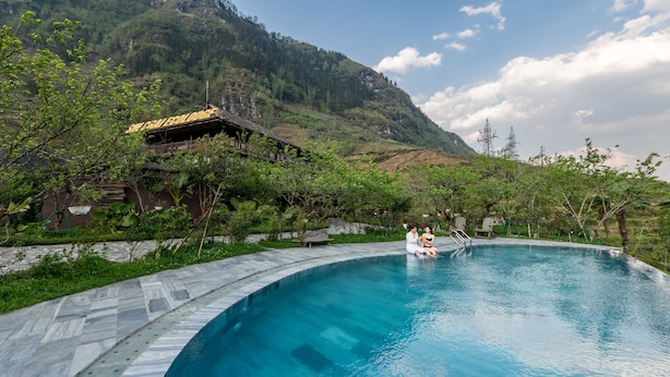 Una piscina de borde curvo, rodeada de abundante vegetación y un telón de fondo montañoso.