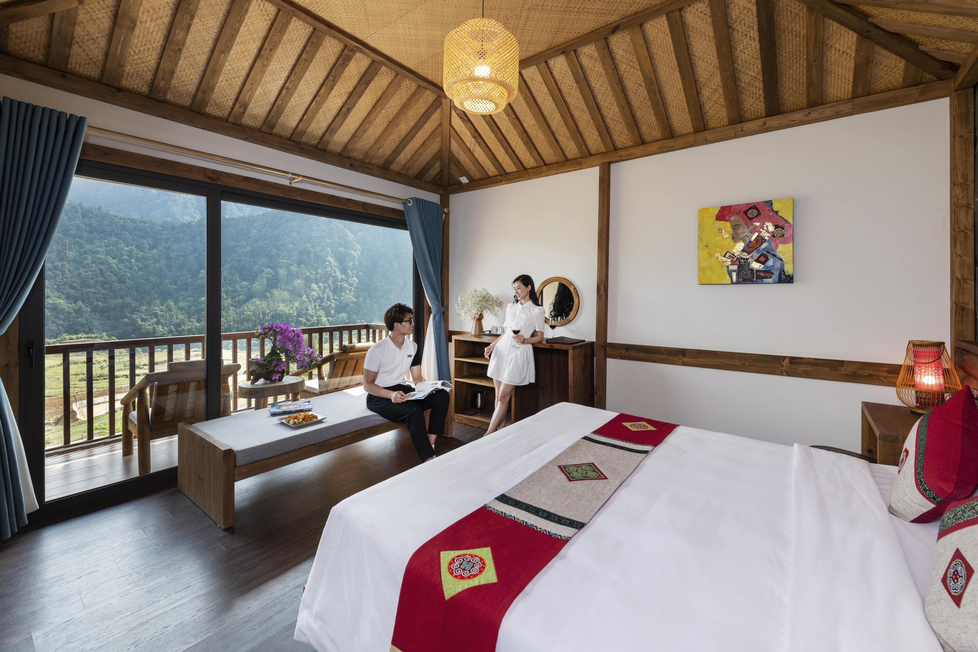 A hotel room with a large bed, a wooden ceiling, a dining table, and a view of the mountains.