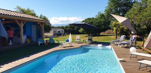 A swimming pool with lounge chairs and umbrellas, a covered patio, and a view of mountains in the background. - Peace and green charm (Salies-du-Salat)