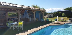 A covered patio area with outdoor furniture, a swimming pool, and a view of mountains in the background. - Peace and green charm (Salies-du-Salat)