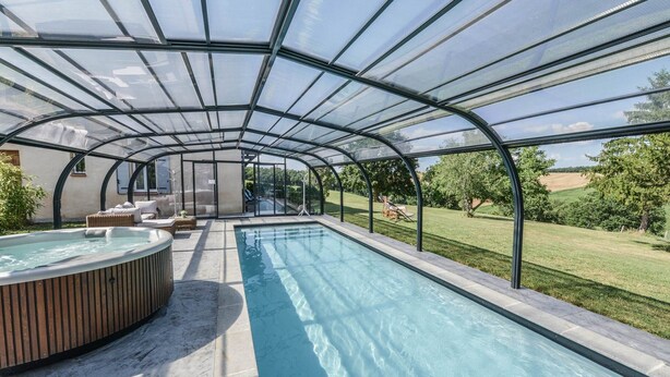 Une piscine couverte avec un jacuzzi, des chaises longues et une vue sur la campagne.