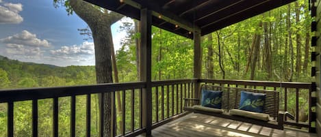 A wooden deck with a bench and cushions, overlooking a forested area.