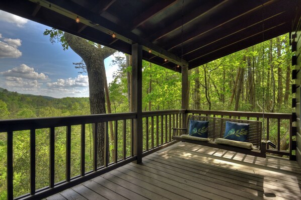 A wooden deck with a bench and cushions, overlooking a forested area.