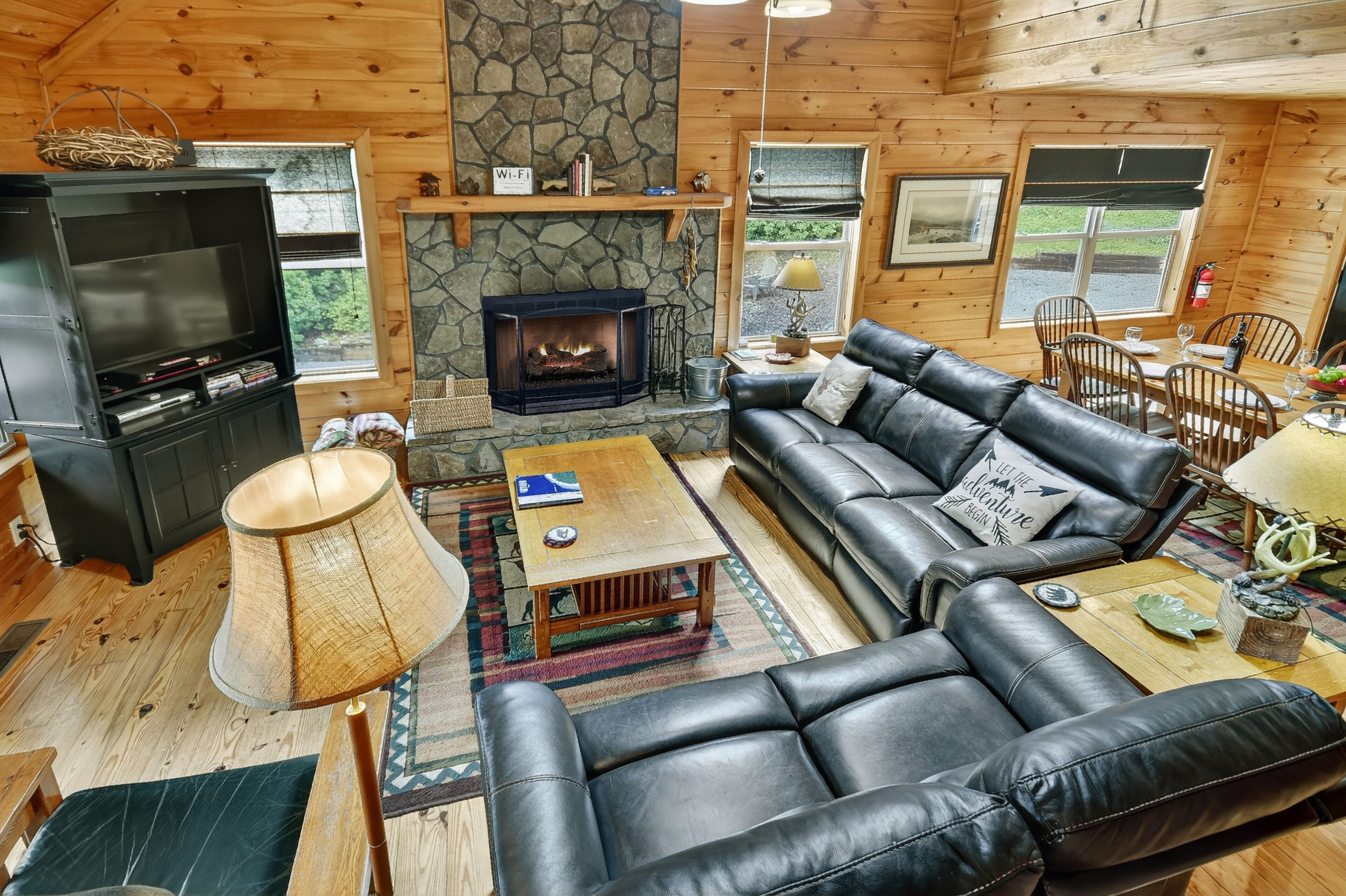 A cozy cabin interior with a stone fireplace, leather sofa, and a television.