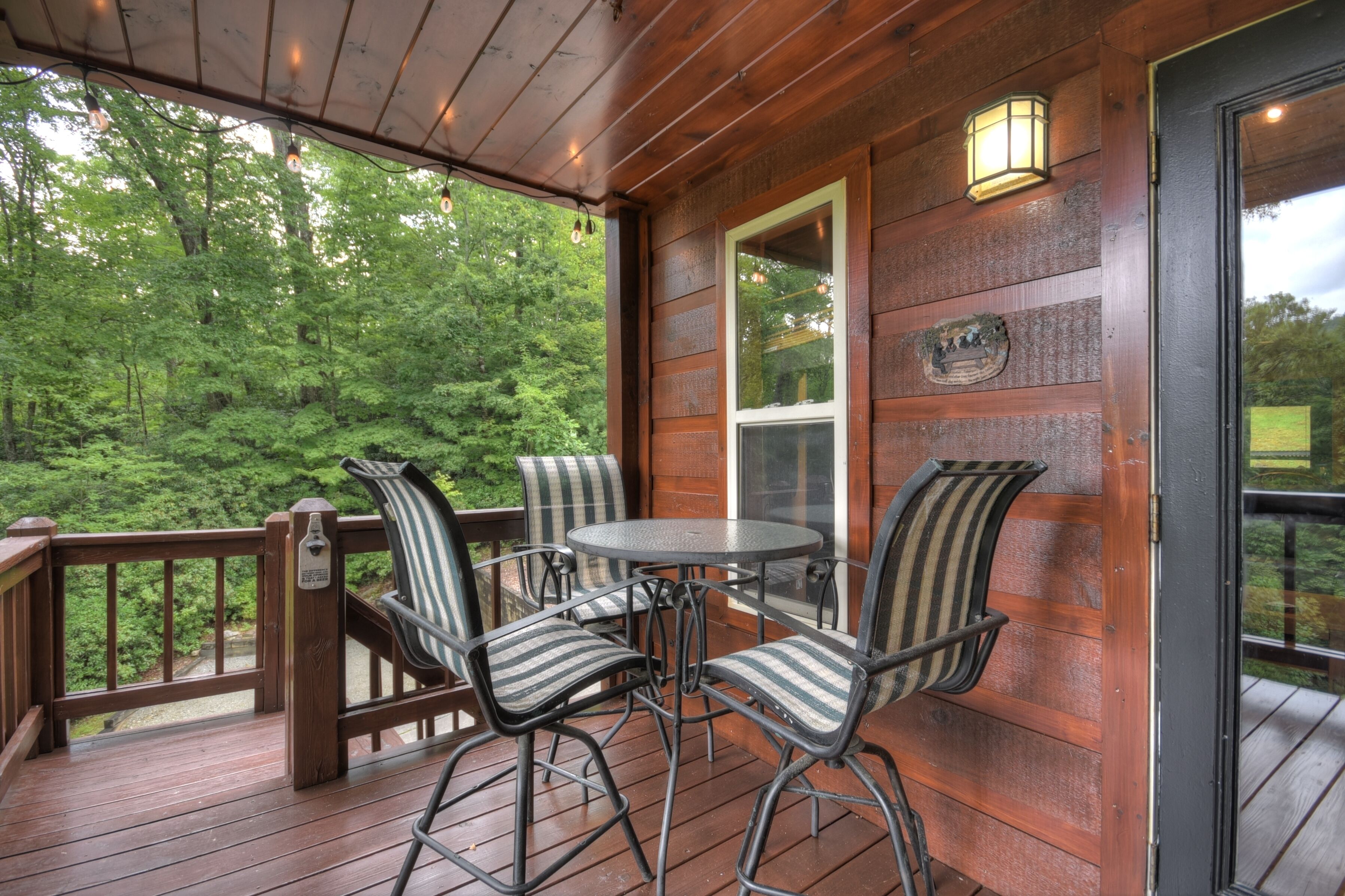A wooden deck with a table and chairs, a glass door, and a view of a forest.