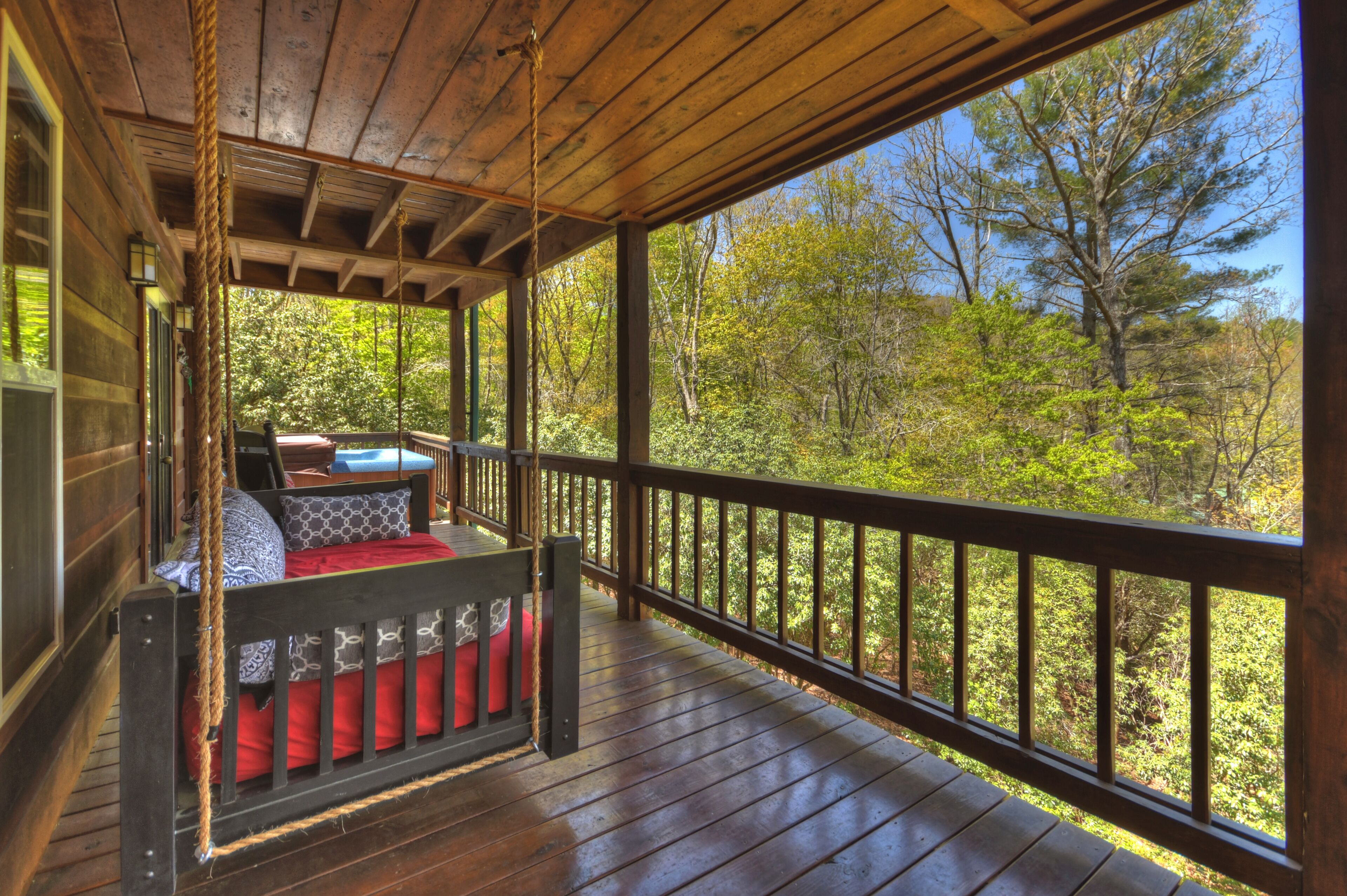 Una terraza de madera con un asiento tipo columpio y vistas a un bosque.