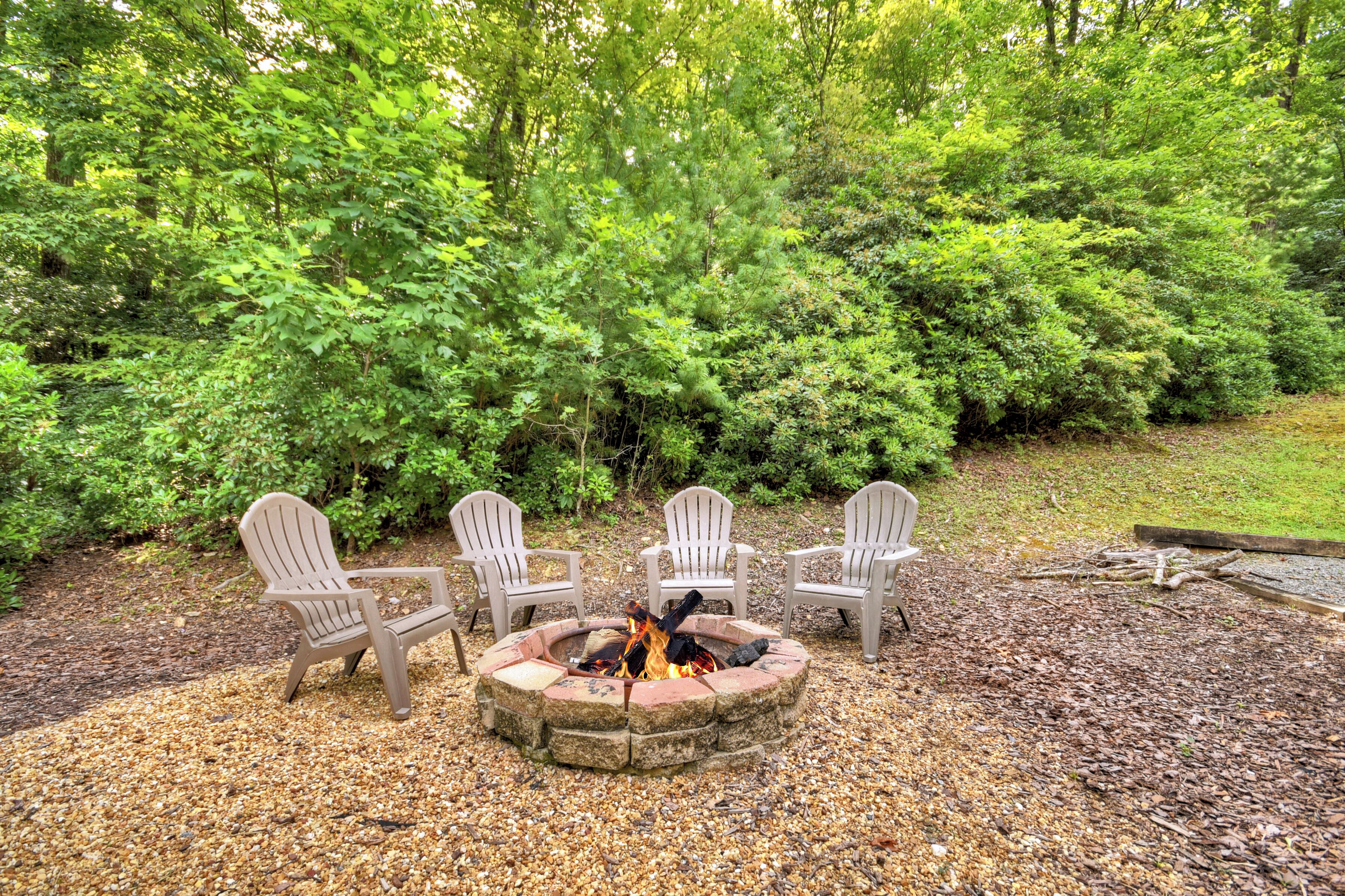 A fire pit with three Adirondack chairs in a forested area.