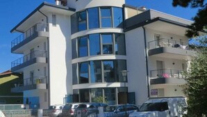 Un edificio de varios pisos con balcones, un estacionamiento y un cielo azul despejado.