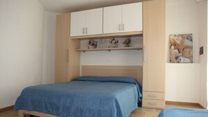 Un dormitorio con cama, armario y repisa con objetos decorativos.