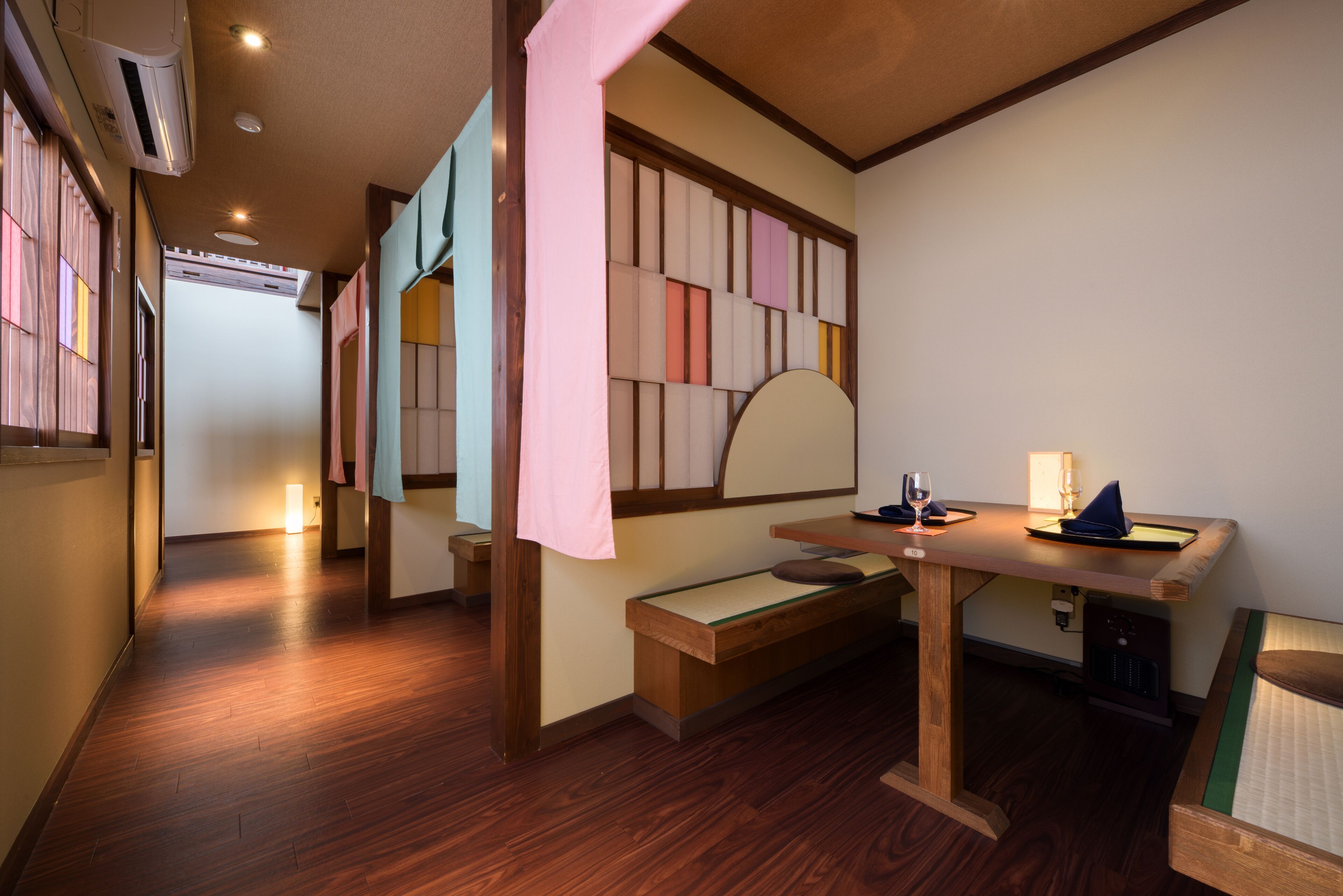 Habitación de hotel con piso de madera, un escritorio con lámpara, una silla y una cama con cabecera verde.