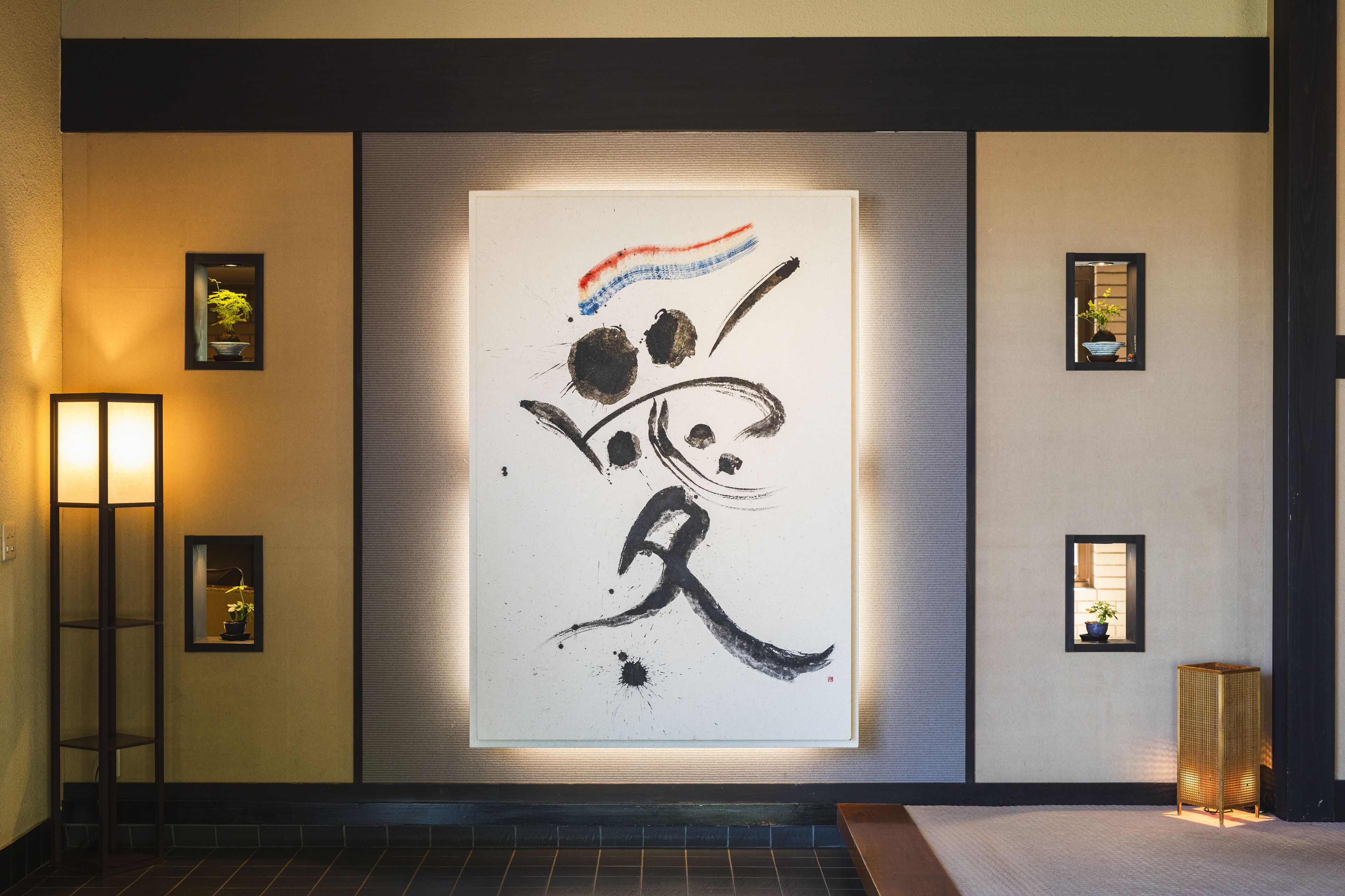 A wall with a large calligraphy artwork, a ladder, and two small framed pictures.