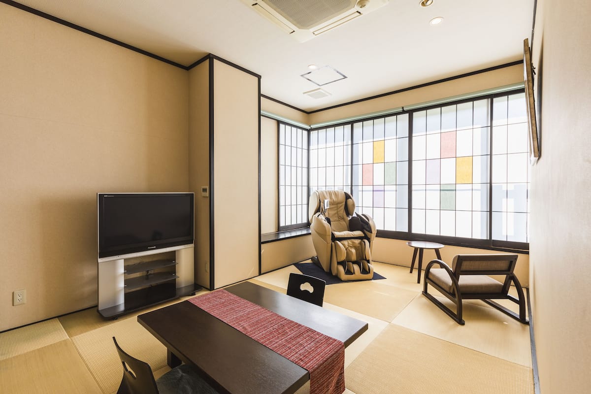 Una habitación con suelo de tatami, televisor de pantalla plana, sillón de masaje y una pequeña mesa.