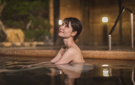 A person sitting in a pool with a wooden edge and a metal railing in the background.