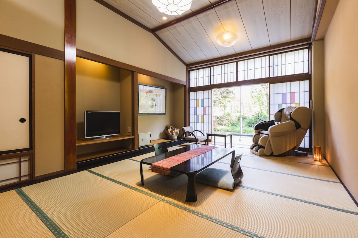 Una habitación japonesa tradicional con suelo de tatami, una mesa baja, un televisor y un sillón de masaje.