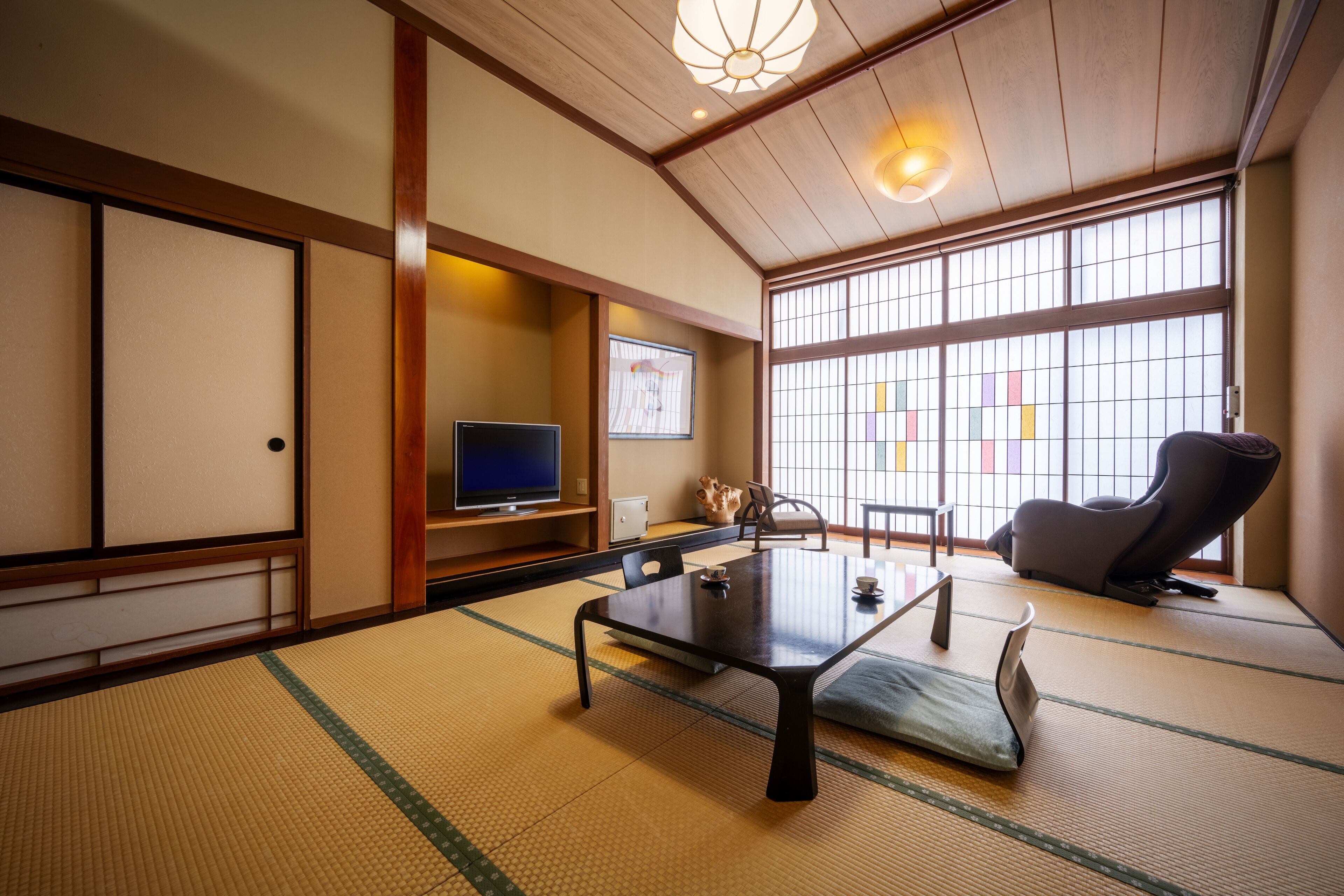 A traditional Japanese room with tatami flooring, a low table, a television, and a massage chair.