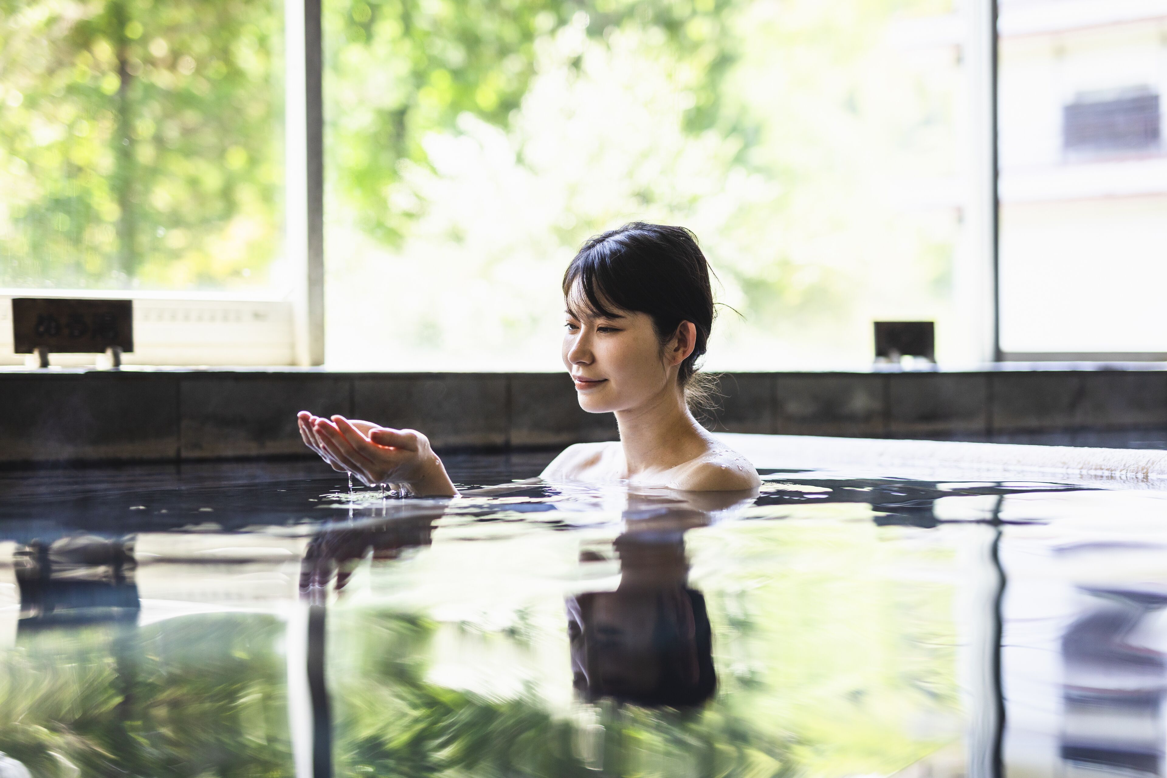 A person in a swimming pool with a view of greenery outside.