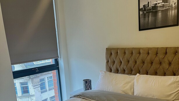 Een hotelkamer met een groot bed, een raam met uitzicht op gebouwen, een hoofdbord en een ingelijst schilderij aan de muur.