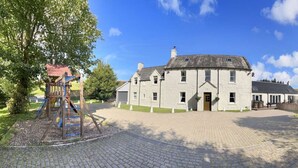 A large stone building with a central entrance, surrounded by a paved courtyard and a wooden fence.
