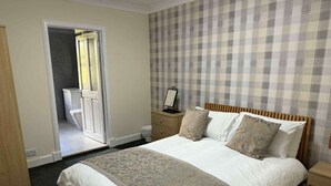 A bedroom with a large bed, a wooden headboard, a bedside table with a lamp, and a plaid-patterned wall.