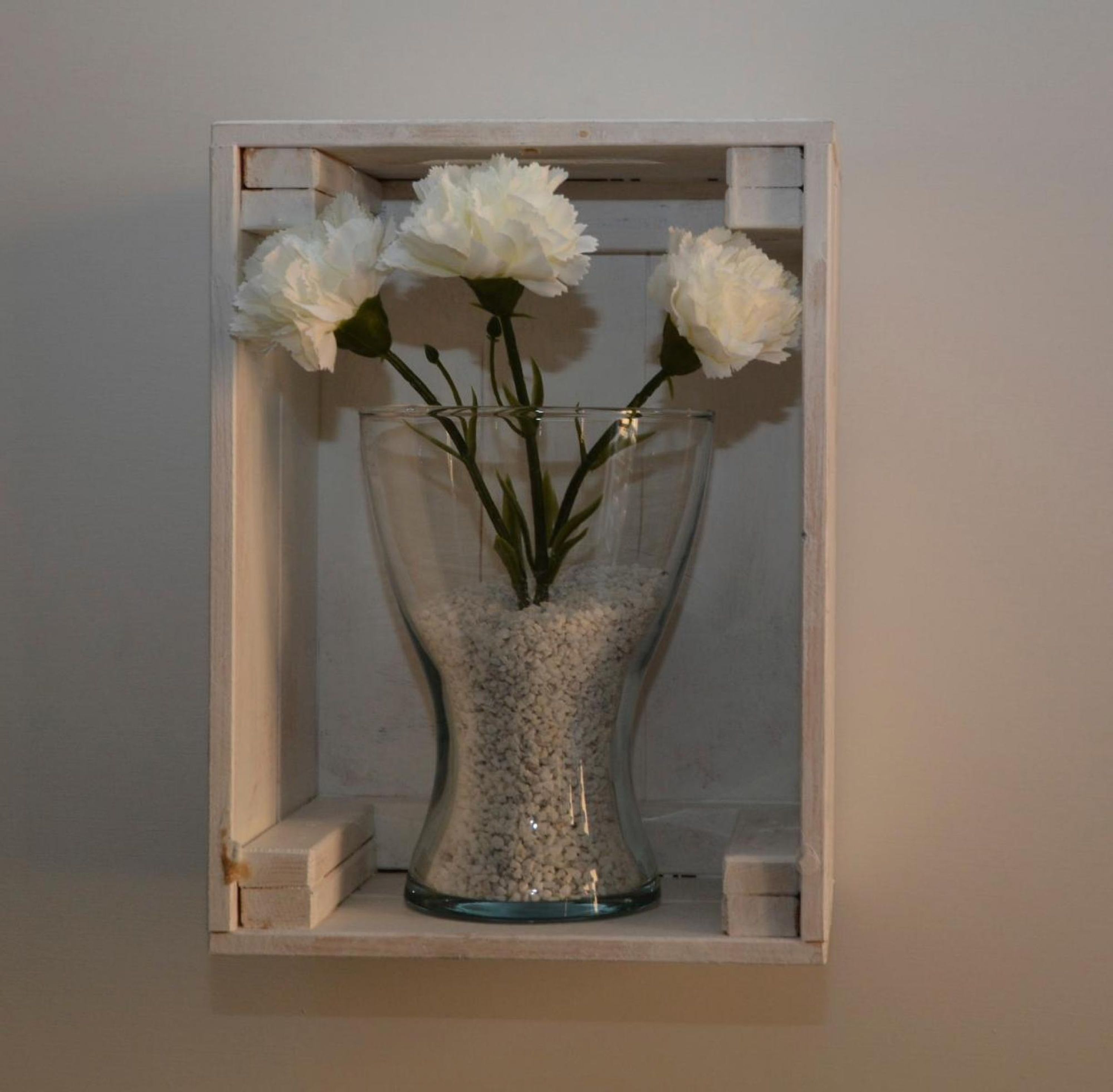 A clear glass vase with white flowers on a shelf.