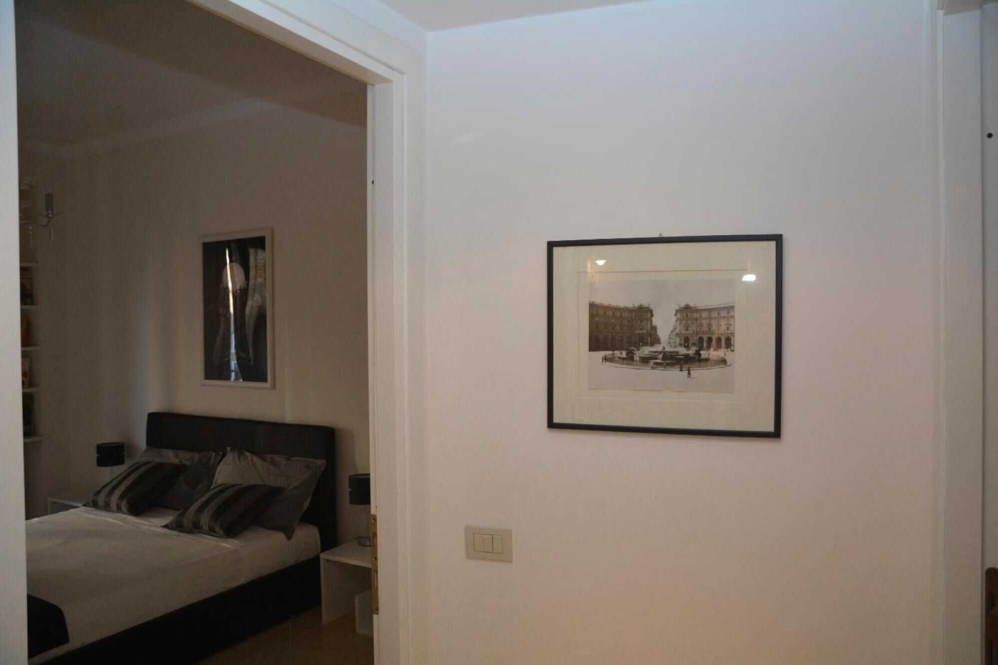 A bedroom with a bed, a nightstand, a wall-mounted light, and a framed picture on the wall.