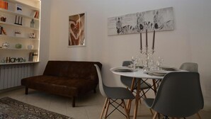 Una sala de estar moderna con un sofá marrón, una mesa de comedor preparada para cuatro personas y una estantería con diversos objetos.