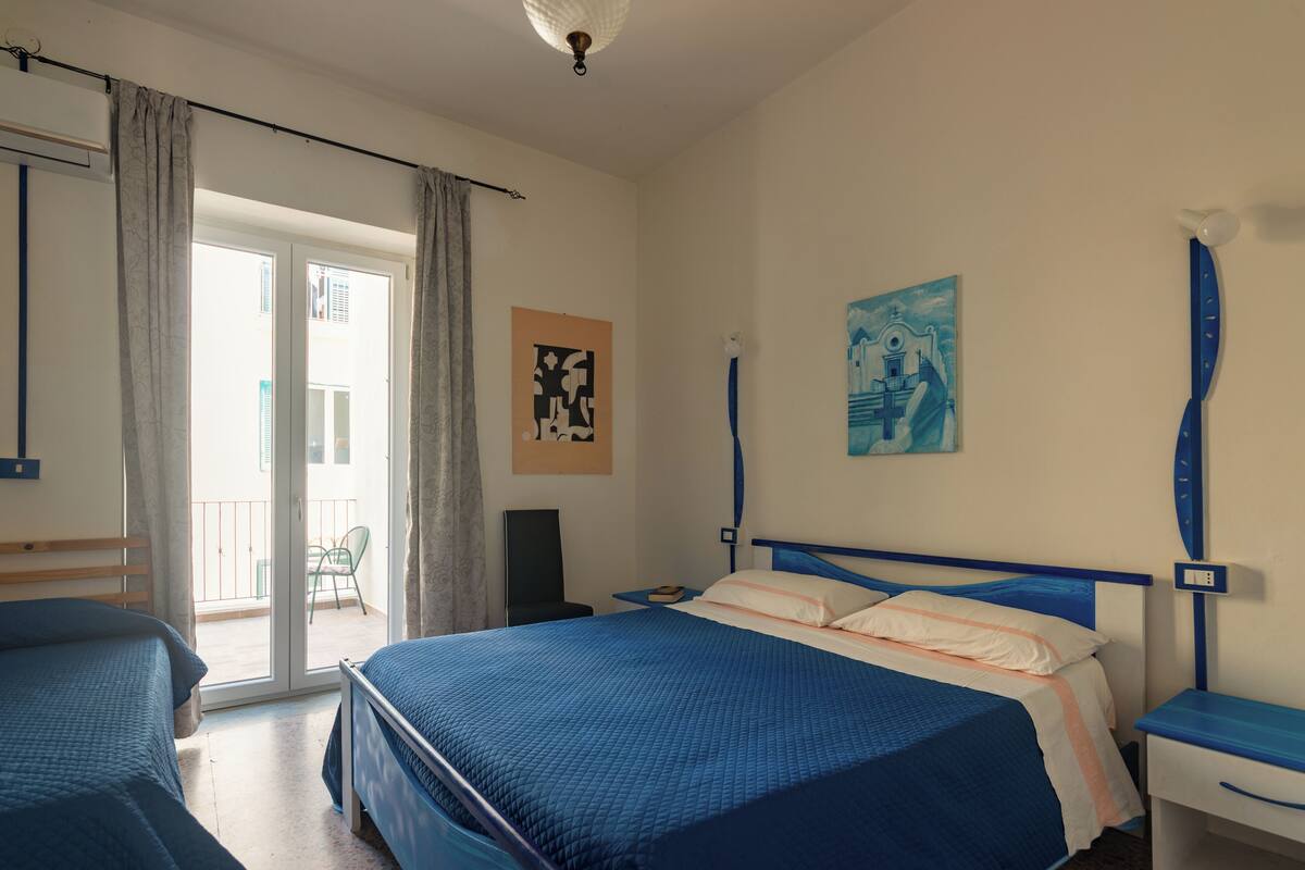 A hotel room with two beds, a balcony, a painting, and a clock on the wall.
