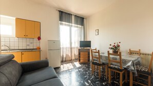 A compact living space with a kitchenette, a dining area with a table and chairs, a sofa, and a television. - Villa dei Sogni (Ischia)