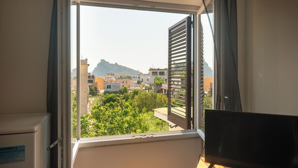 A room with a window offering a view of buildings and greenery. - Villa dei Sogni (Ischia)