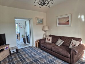 A living room with a brown leather sofa, a plaid carpet, a television, and a chandelier.