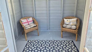 A covered porch with two wicker chairs, each with a pillow, and a patterned rug on the floor. - Beautiful 2-bed Semi Rural Cottage Enclosed Garden (Stranraer)