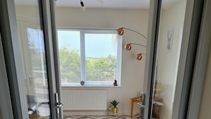 A room with a herringbone floor, a brown leather sofa, a small table with a lamp, and a window with blinds. - Beautiful 2-bed Semi Rural Cottage Enclosed Garden (Stranraer)