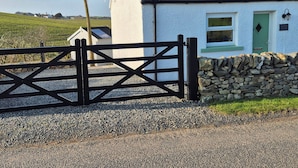 A white building with a green door, a stone wall, and a black gate. - Beautiful 2-bed Semi Rural Cottage Enclosed Garden (Stranraer)