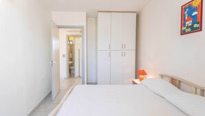 Een slaapkamer met een bed, een kledingkast, een nachtkastje met een lamp, en een badkamer die door een open deur zichtbaar is.