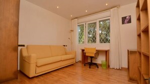 A room with a wooden floor, a beige sofa, a desk with a chair, and a window with curtains. - Beautiful villa  in Platja d´Aro with sea views and a pool (Platja d'Aro)