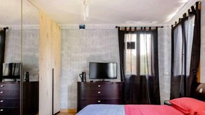 A bedroom with a bed, a TV on a stand, a wardrobe, and a mirror.