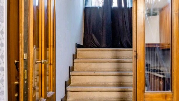 A wooden staircase leading to a room with a window and curtains.