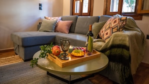 A cozy living room with a sectional sofa, a wooden coffee table with fruits and a bottle, and a window with patterned curtains. - Dandy Villas Ioannina- Colorful Boutique House (Ioannina)